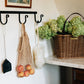 Hanging hooks with a net bag, broom, and duster against a wall with a basket of flowers on a shelf.