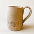 A handmade ceramic mug with a textured, organic shape and embossed floral pattern near the base, shown on a neutral beige background.
