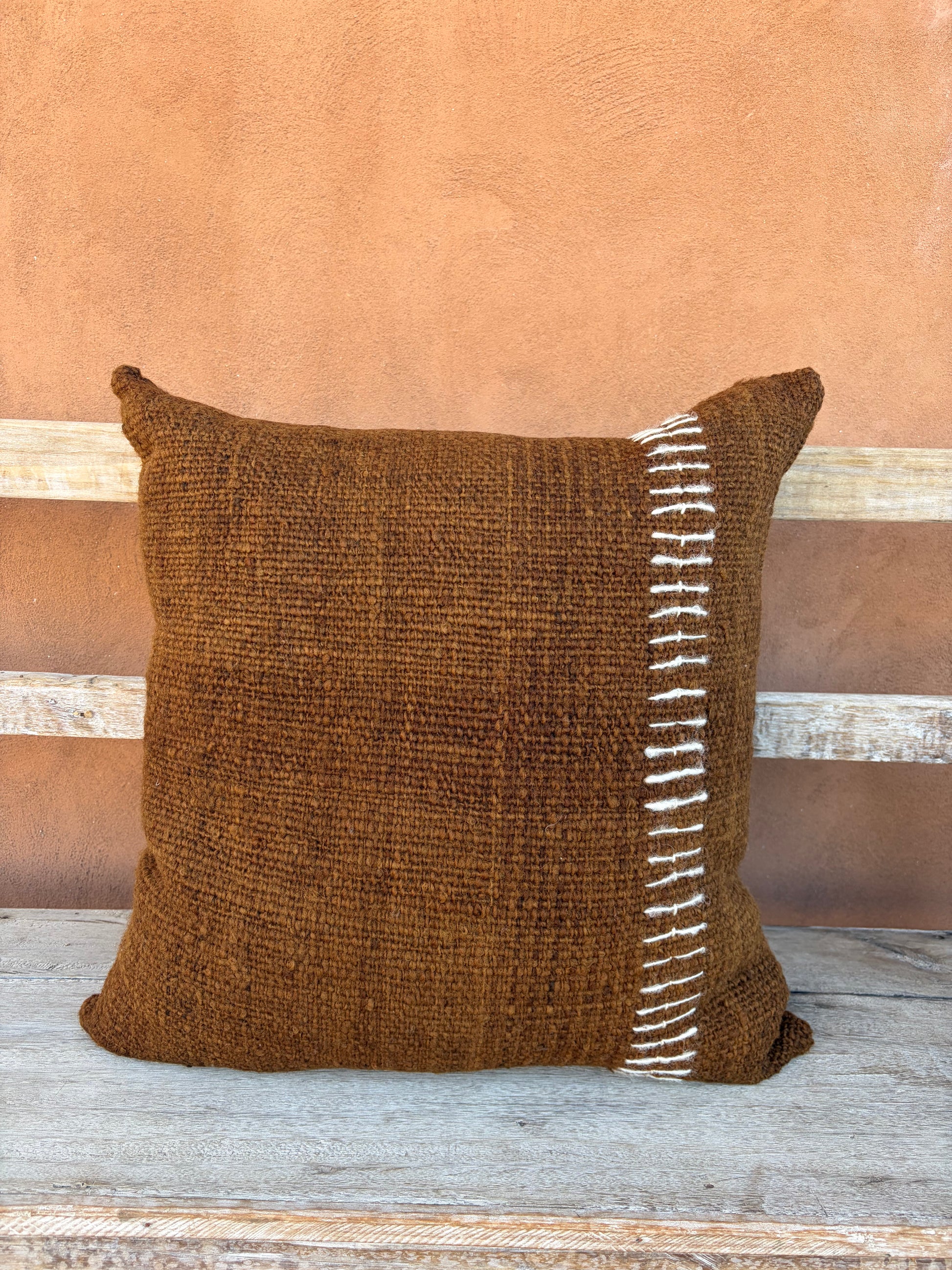 Brown pillow with white decorative stripe on a wooden surface with a brown background