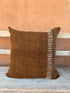 Brown pillow with white decorative stripe on a wooden surface with a brown background