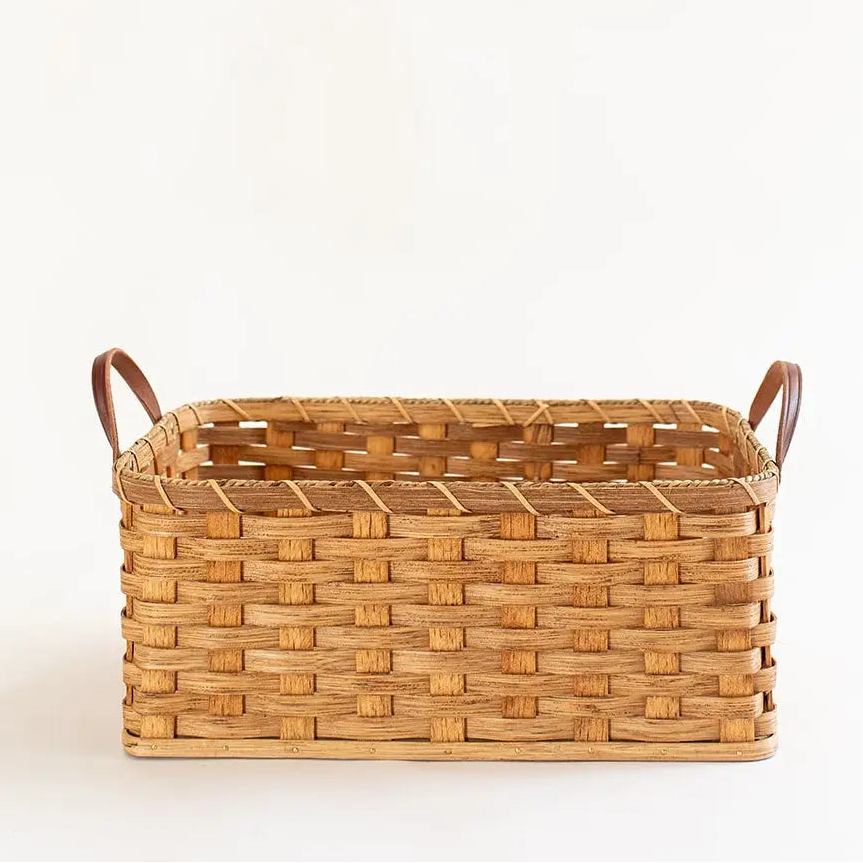 A rectangular woven basket with two brown leather handles, shown on a clean white background.