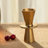 Gold metallic cup on a matching stand with two cherries on a textured surface.